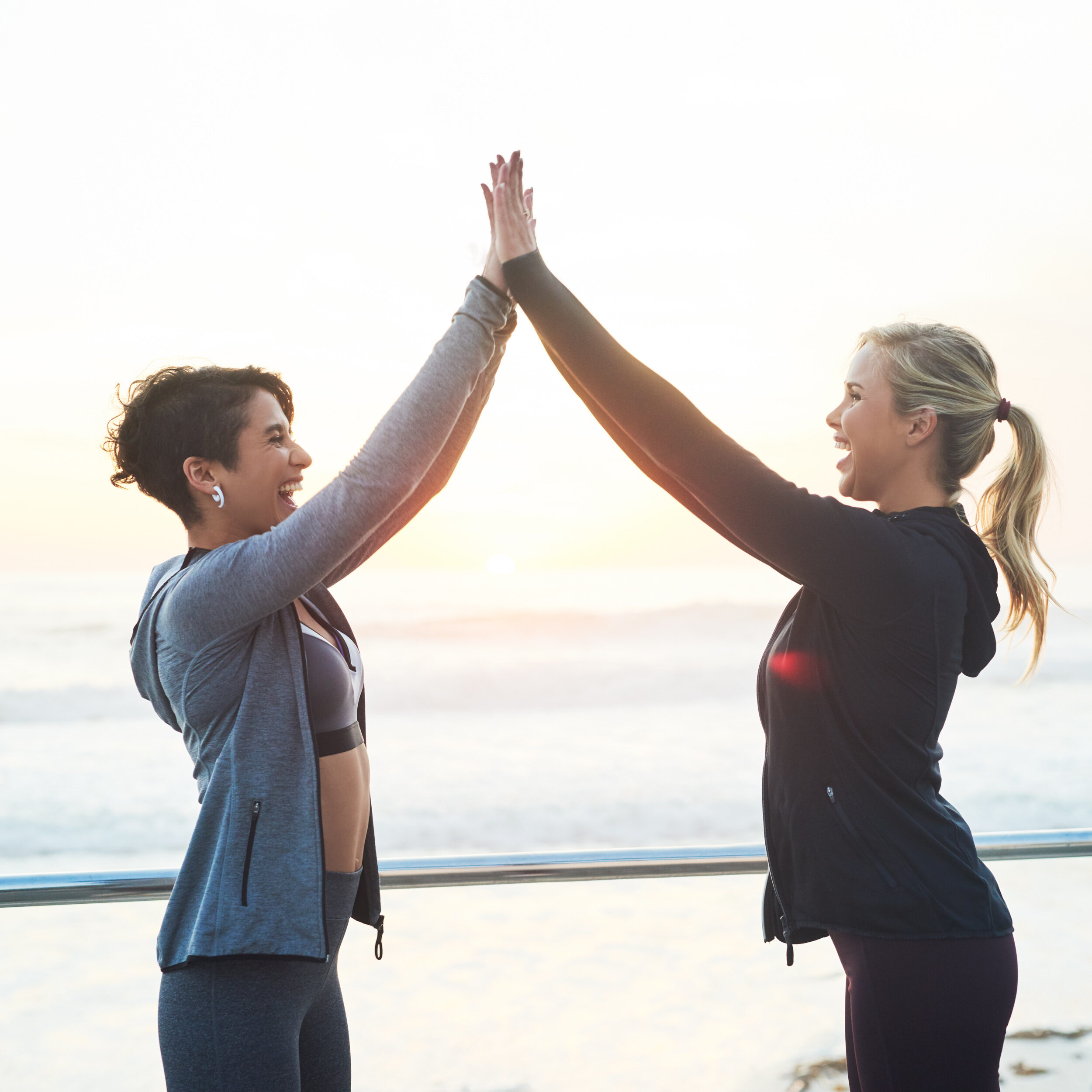 High five, friends and smile on run, outdoor and routine for fitness in morning, beach and healthy with workout. Sea, women and wellness with exercise in nature, sports and bonding with celebration.